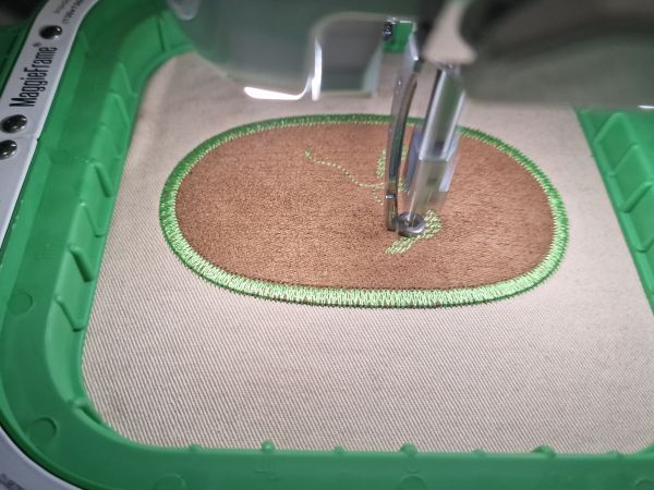 Réparation d'une manche de pantalon. Une pièce de réparation ovale est fixée par une bordure en double zigzag.